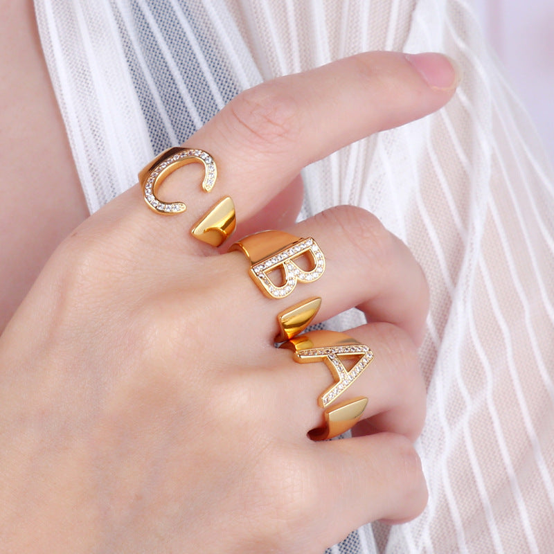 Adjustable brass letter A ring with micro-paved zirconia stones close-up, Top view of 18K gold-plated brass alphabet ring set spread on velvet, Side view of brass letter D ring worn on finger with adjustable opening, Macro shot of zirconia stone details and brass texture on alphabet ring, 
