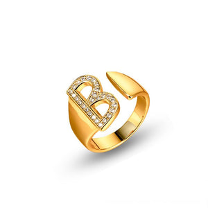 Adjustable brass letter A ring with micro-paved zirconia stones close-up, Top view of 18K gold-plated brass alphabet ring set spread on velvet, Side view of brass letter D ring worn on finger with adjustable opening, Macro shot of zirconia stone details and brass texture on alphabet ring, 